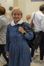 Uśmiechnięta słuchaczka w jeansowej sukience z białym koronkowym kołnierzykiem trzyma pasek czarnego tornistra