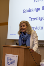 Kierowniczka Trzeciego Wieku podczas przemówienia. Stoi przy mównicy.